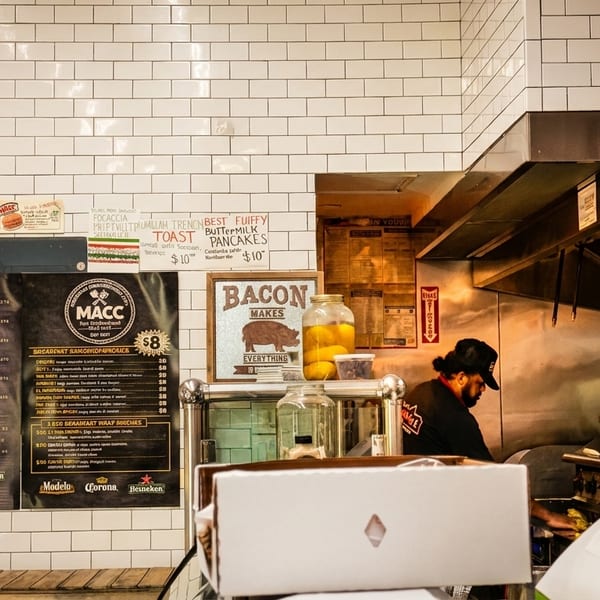 A chef works in a busy kitchen with white subway tile walls and a menu board.