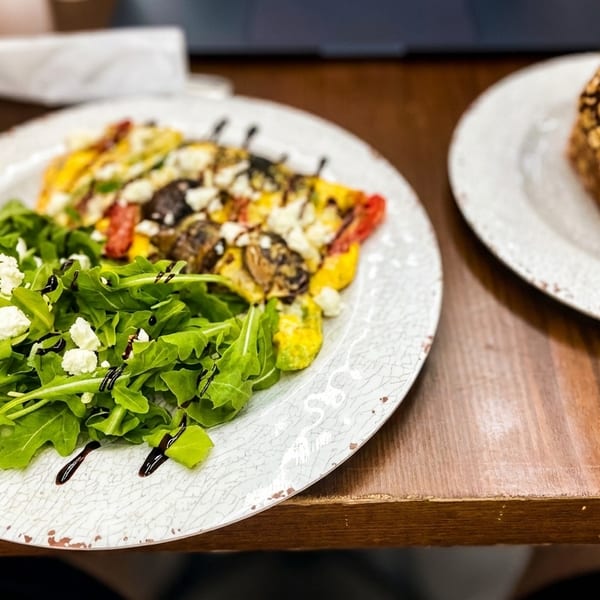 A colorful omelet with arugula salad and a side of whole-grain bread on a wooden table.