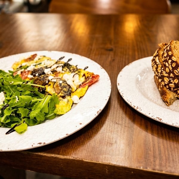A breakfast plate with an omelet, arugula salad, and a side of multigrain toast.