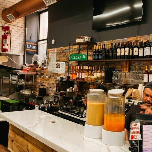 A man stands behind a counter with drinks and wine bottles in a restaurant kitchen.