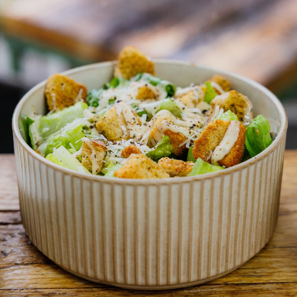 Crisp green salad topped with breaded chicken, croutons, grated cheese, and creamy dressing in a ceramic bowl.